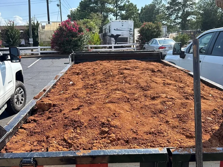 Dump trailer loaded with excavated red clay spoil from an interior grease trap dig