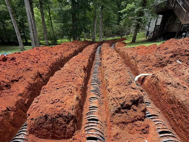 Wide view of a multi-line residential drain field replacement on a wooded sloping lot